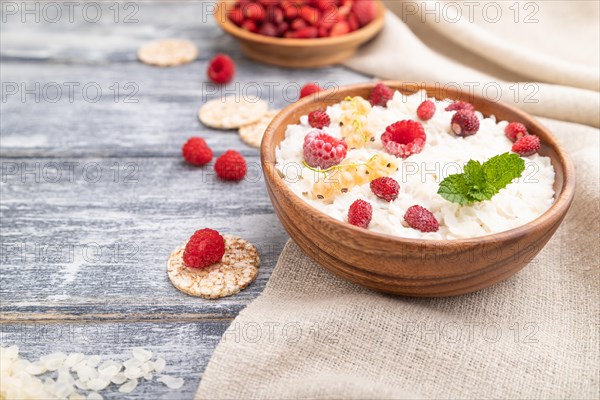 Rice flakes porridge with milk and strawberry in wooden bowl on gray wooden background and linen textile. Side view, selective focus, close up
