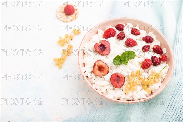 Rice flakes porridge with milk and strawberry in ceramic bowl on white concrete background and blue linen textile. Side view, close up, selective focus