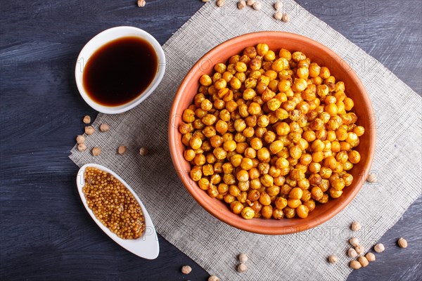 Fried chickpeas with spices in a clay plate on black wooden background, top view, copy space