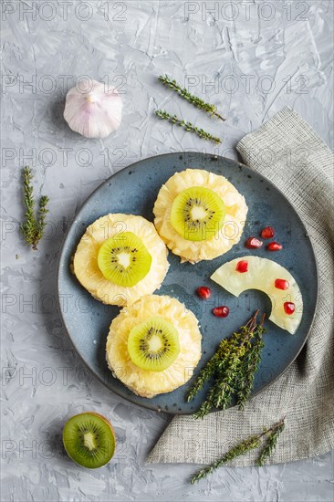 Pieces of baked pork with pineapple, cheese and kiwi on gray background, top view