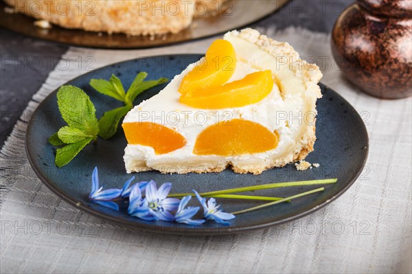 A piece of peach cheesecake on a blue ceramic plate with blue flowers and a cup of coffee on a linen napkin on a black concrete background. side view, close up, selective focus