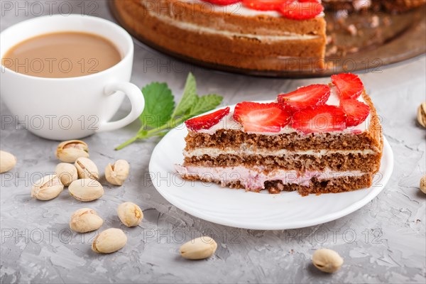 Homemade cake with yoghurt cream, strawberry, pistachio and a cup of coffee on a gray concrete background. side view, selective focus, close up