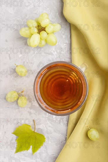 Glass of green grape juice with green textile on a gray concrete background. Morninig, spring, healthy drink concept. Top view, close up, flat lay