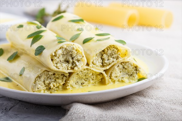 Cannelloni pasta with egg sauce, cream cheese and oregano leaves on a gray concrete background with linen textile. side view, close up, selective focus