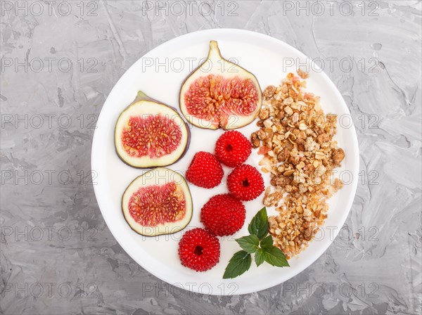 Yoghurt with raspberry, granola and figs in white plate on a gray concrete background top view, flat lay, close up
