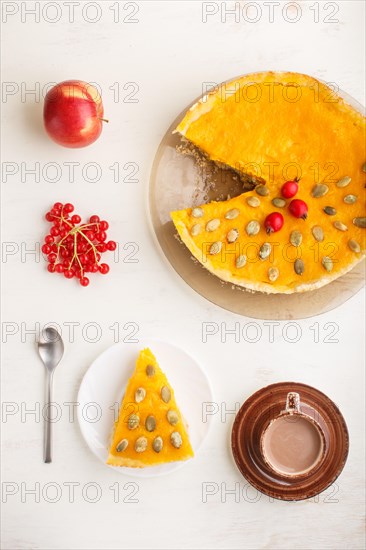 Traditional american sweet pumpkin pie decorated with hawthorn red berries and pumpkin seeds with cup of coffee on a white wooden background. top view, flat lay, close up