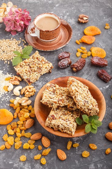 Homemade granola from oat flakes, dates, dried apricots, raisins, nuts with a cup of coffee on a black concrete background. Side view, close up