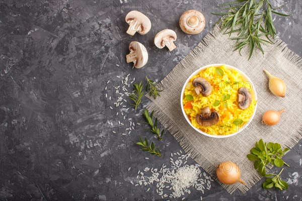 Yellow fried rice with champignons mushrooms, turmeric and oregano in white ceramic bowl on a black concrete background. Top view, flat lay, copy space