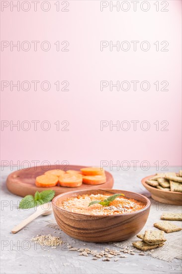 Carrot cream soup with sesame seeds and snacks in wooden bowl on a gray and pink background with linen textile. side view, copy space