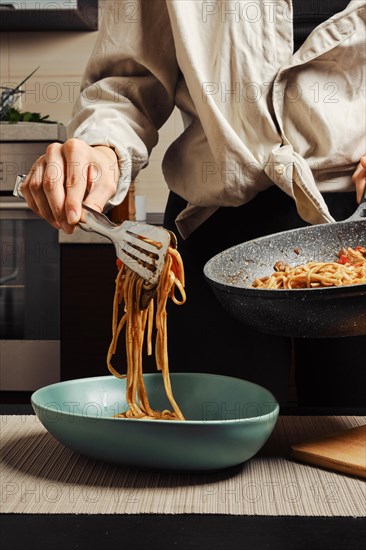 Unrecognizable woman serving rice noodles with vegetables and beef from frying pan into plate