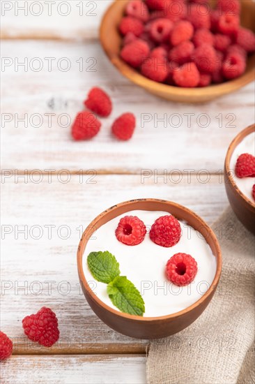 Yogurt with raspberry in clay cups on white wooden background and linen textile. Side view, close up, selective focus