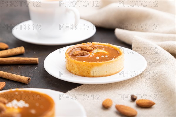 Sweet tartlets with almonds and caramel cream with cup of coffee on a black concrete background and linen textile. Side view, close up, selective focus