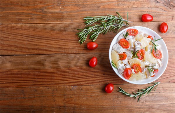 Chicken fillet salad with rosemary, pineapple and cherry tomatoes on brown wooden background. top view, copy space