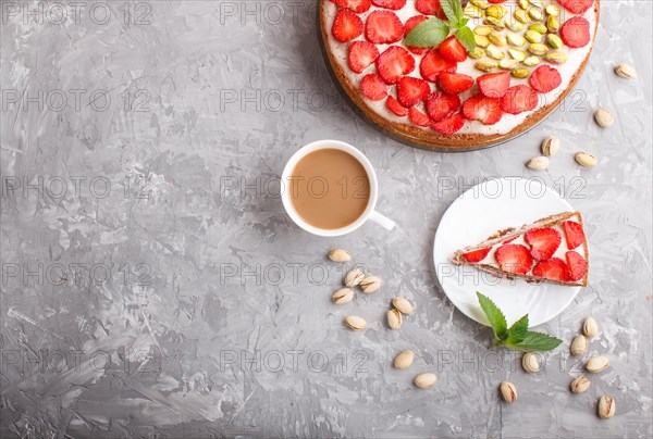 Homemade cake with yoghurt cream, strawberry, pistachio and a cup of coffee on a gray concrete background. top view. flat lay, copy space