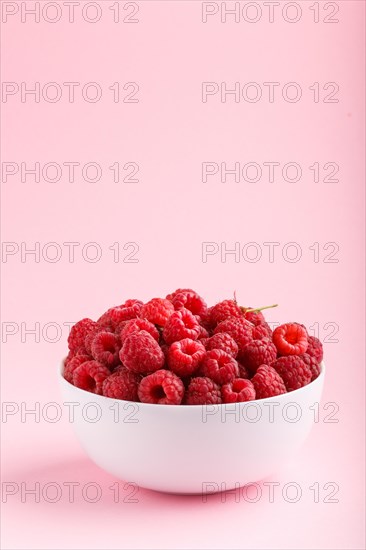 Fresh raspberry in white bowl on pink pastel background. side view, copy space