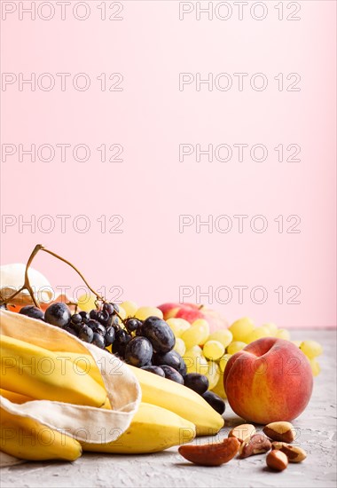 Fruits in reusable cotton textile white bag. Zero waste shopping, storage and recycling concept, eco friendly lifestyle. Side view, close up, copy space. Peach, apple, banana, grape