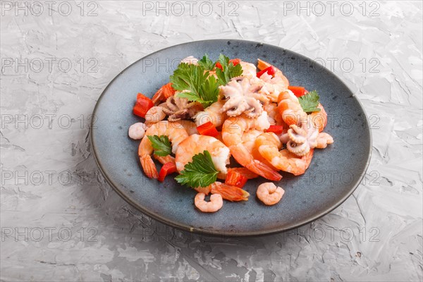 Boiled shrimps or prawns and small octopuses with herbs on a blue ceramic plate on a gray concrete background. side view, close up