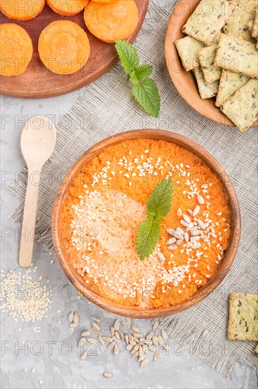 Carrot cream soup with sesame seeds and snacks in wooden bowl on a gray concrete background with linen textile. top view, flat lay, close up