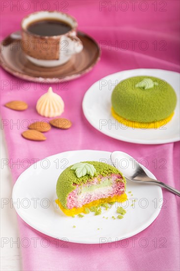 Green mousse cake with pistachio and strawberry cream on a white wooden background and pink textile. side view, close up, selective focus