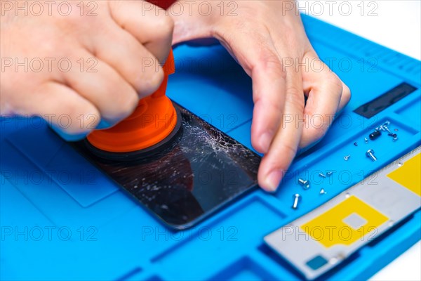 Technician uses a suction cup to lift the screen of a mobile phone in the repair shop