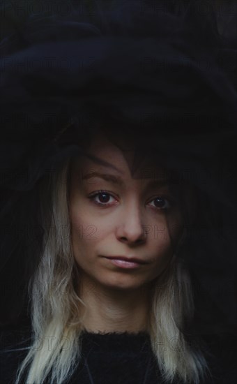 Close-up of a white thin caucasian blonde woman with serious expression, wearing dark clothing