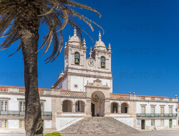 Baroque church under a clear blue sky with surrounding palm trees and a staircase in front Nazareh Portugal