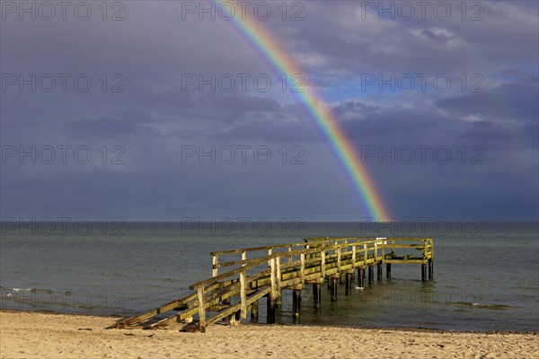 A great rainbow in the evening light over an old wooden pier on the Baltic Sea