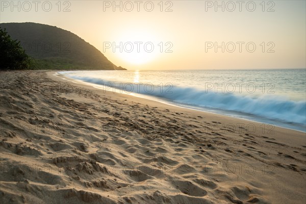 View over a beach, the coast and the sea at sunset. In the foreground the empty sandy beach of Grande Anse, Basse Terre, Guadeloupe, French Antilles, Caribbean, North America