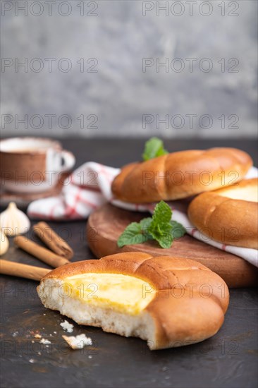 Sour cream bun with cup of coffee on a black concrete background and linen textile. Side view, copy space