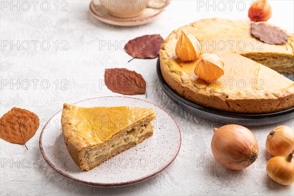 Autumn onion pie decorated with leaves and cup of coffee on gray concrete background. Side view, close up
