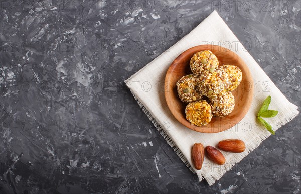 Energy ball cakes with dried apricots, sesame, linen, walnuts and dates with green mint leaves in a wooden bowl on a black concrete background. linen napkin, top view, copy space, flat lay. vegan homemade candy