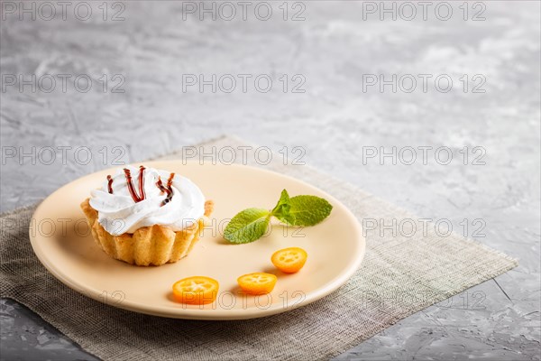Cake with whipped egg cream on a light brown plate with kumquat slices and mint leaves on a gray concrete background with linen napkin. selective focus, copy space, side view