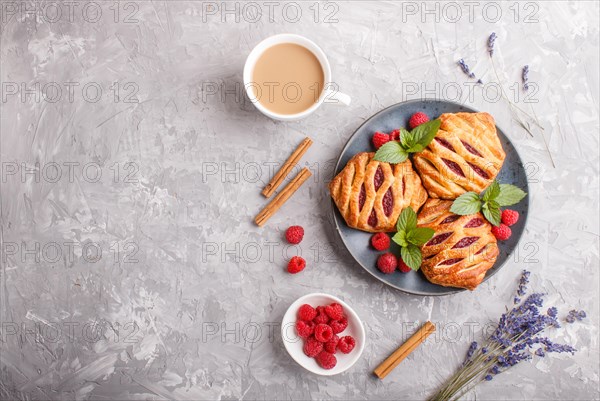 Puff pastry buns with strawberry jam on blue ceramic plate on gray concrete background, cup of coffee, lavender, cinnamon, mint leaves. top view, flat lay, copy space