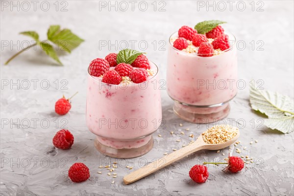 Yoghurt with raspberry and sesame in a glass and wooden spoon on gray concrete background. side view, close up