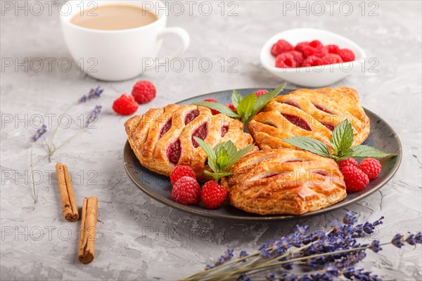 Puff pastry buns with strawberry jam on blue ceramic plate on gray concrete background, cup of coffee, lavender, cinnamon, mint leaves. side view, close up, selective focus