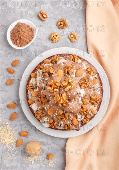 Homemade cake with milk cream, cocoa, almond, hazelnut on a gray concrete background with orange textile. Top view, flat lay