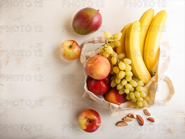 Fruits in reusable cotton textile white bag. Zero waste shopping, storage and recycling concept, eco friendly lifestyle. Top view, flat lay, copy space. Peach, apple, mango, grape, banana
