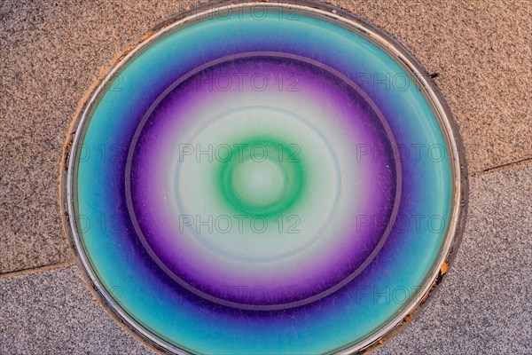 Closeup round glass of blue, green and purple inlaid in concrete sidewalk in public park in South Korea
