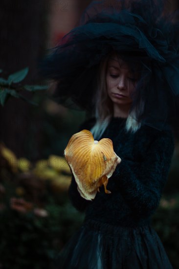 Woman in a hat holding a large mushroom amidst an autumn forest setting