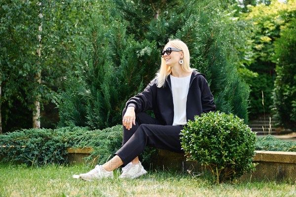 Woman in black hoodie and fleece trousers rests on backyard