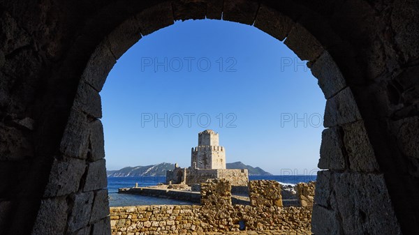 View from an arch onto an old stone watchtower spire in front of a picturesque sea panorama, octagonal medieval tower. Islet of Bourtzi, sea fortress of Methoni, Peloponnese, Greece, Europe