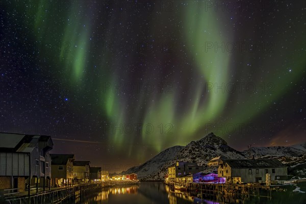 Polarlichter ueber einem beleuchteten und verschneiten Fischerdorf auf den Vesteralen