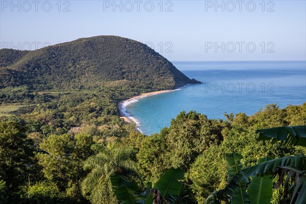 View from a mountain onto an empty sandy beach, the turquoise-coloured sea and the surrounding landscape. The morning sun illuminates the natural surroundings of Grande Anse Beach, Basse Terre, Guadeloupe, the French Antilles and the Caribbean in a unique way at sunrise, North America