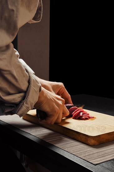 Closeup of hands of unrecognizable woman slicing raw beef meat on thin slices