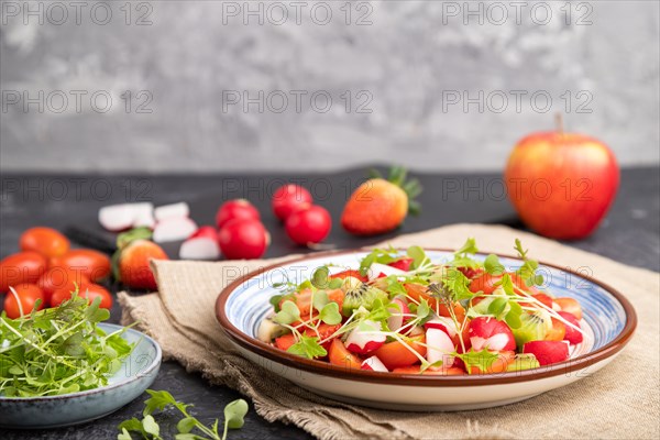 Vegetarian fruits and vegetables salad of strawberry, kiwi, tomatoes, microgreen sprouts on black and gray background and linen textile. Side view, selective focus, copy space
