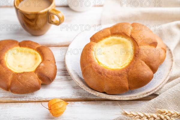 Sour cream bun with cup of coffee on a white wooden background and linen textile. Side view, close up, selective focus