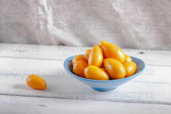 Kumquats in a blue plate on a white wooden background, close up