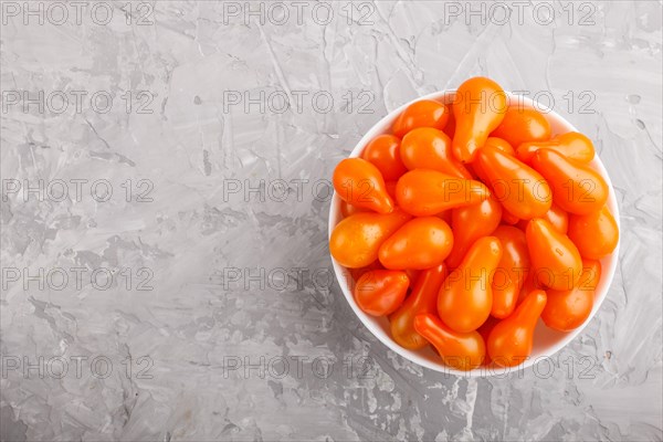 Fresh orange grape tomatoes in white ceramic bowl on gray concrete background. top view, flat lay, copy space