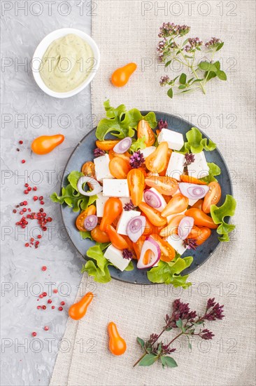 Vegetarian salad with fresh grape tomatoes, feta cheese, lettuce and onion on blue ceramic plate on gray concrete background and linen textile. top view, flat lay