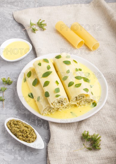 Cannelloni pasta with egg sauce, cream cheese and oregano leaves on a gray concrete background with linen textile. side view, close up